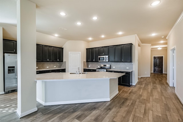 kitchen with crown molding, an island with sink, tasteful backsplash, wood-type flooring, and stainless steel appliances