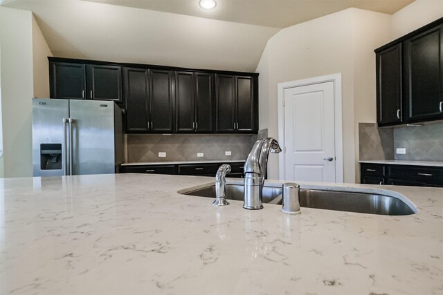 kitchen with light stone countertops, lofted ceiling, stainless steel refrigerator with ice dispenser, and tasteful backsplash