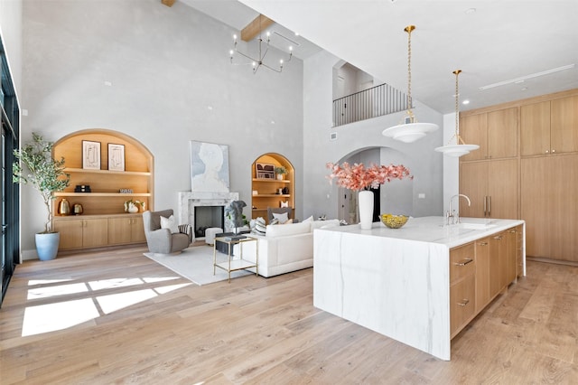 kitchen with pendant lighting, a high ceiling, an island with sink, built in features, and sink