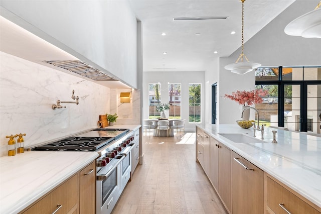 kitchen with light stone countertops, pendant lighting, double oven range, sink, and backsplash