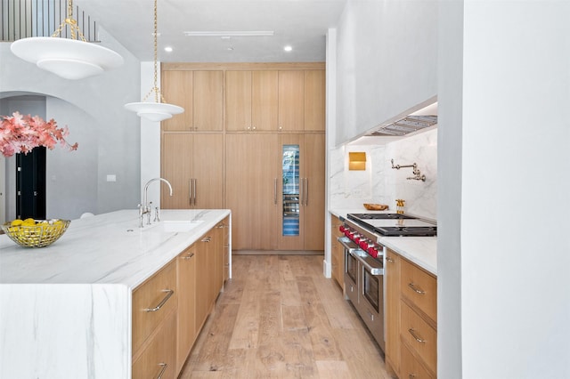 kitchen with sink, a large island with sink, range with two ovens, light stone countertops, and pendant lighting