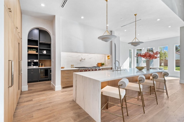 kitchen featuring decorative light fixtures, light hardwood / wood-style floors, a kitchen bar, a large island, and sink