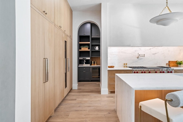 interior space with decorative light fixtures, light hardwood / wood-style floors, beverage cooler, stainless steel gas cooktop, and backsplash