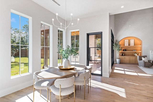 dining room featuring built in shelves, an inviting chandelier, a wealth of natural light, and light hardwood / wood-style floors