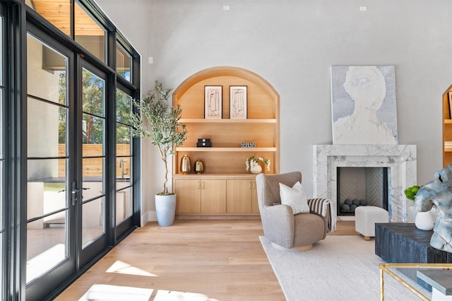 living area featuring a towering ceiling, french doors, built in features, light hardwood / wood-style flooring, and a high end fireplace