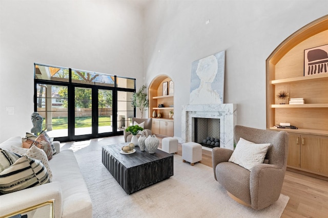 living room featuring a towering ceiling, built in shelves, a premium fireplace, and light wood-type flooring