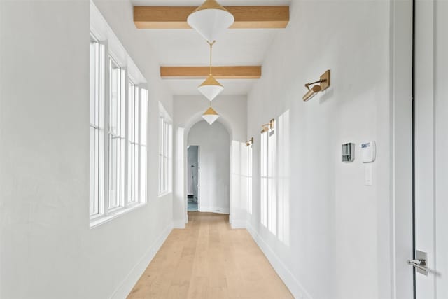 hallway with light hardwood / wood-style floors, beamed ceiling, and plenty of natural light