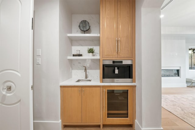 bar with sink, beverage cooler, light hardwood / wood-style floors, and oven