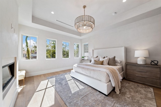 bedroom with an inviting chandelier, a tray ceiling, and light hardwood / wood-style flooring