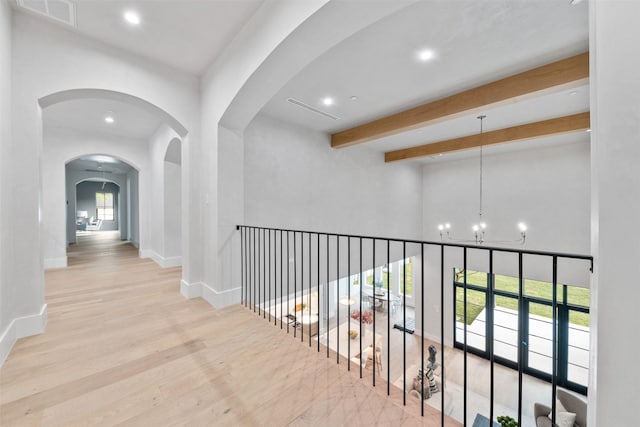 corridor with an inviting chandelier, beam ceiling, and light wood-type flooring