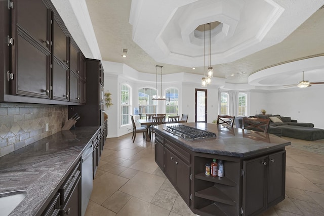 kitchen featuring tasteful backsplash, ceiling fan with notable chandelier, a raised ceiling, a kitchen island, and hanging light fixtures