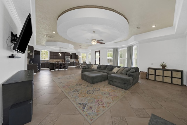 tiled living room featuring a raised ceiling, ceiling fan, and crown molding