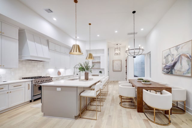 kitchen with decorative light fixtures, sink, white cabinets, high end stainless steel range oven, and custom exhaust hood