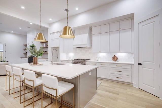 kitchen featuring sink, range, white cabinetry, premium range hood, and a center island with sink