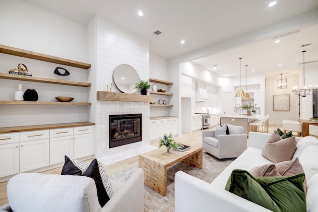 living room with a tile fireplace, sink, a chandelier, and light hardwood / wood-style flooring