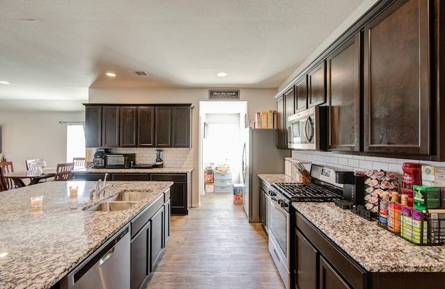 kitchen with light stone counters, dark brown cabinets, stainless steel appliances, sink, and light hardwood / wood-style flooring