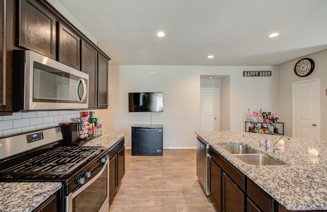 kitchen with dark brown cabinetry, sink, light hardwood / wood-style flooring, decorative backsplash, and appliances with stainless steel finishes