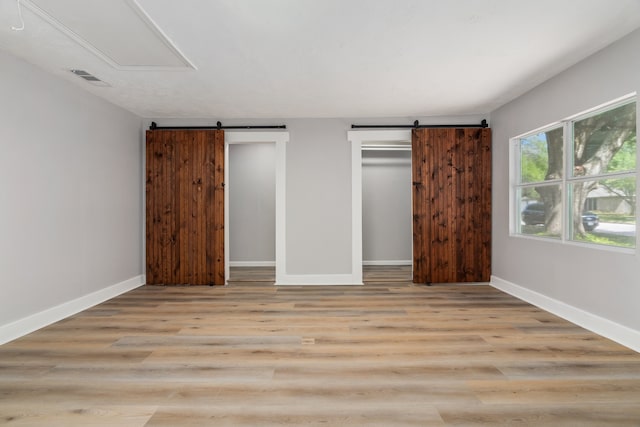 unfurnished bedroom with a barn door and light hardwood / wood-style floors