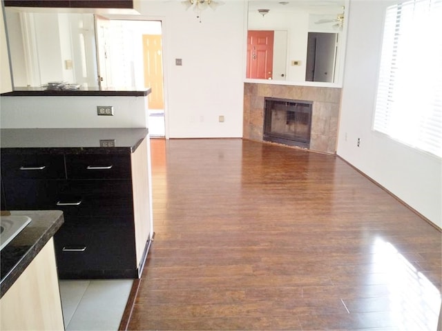 living room featuring ceiling fan, dark hardwood / wood-style flooring, a tile fireplace, and a wealth of natural light