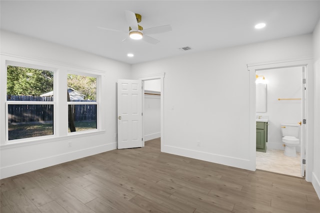 unfurnished bedroom with a walk in closet, ensuite bathroom, ceiling fan, hardwood / wood-style flooring, and a closet