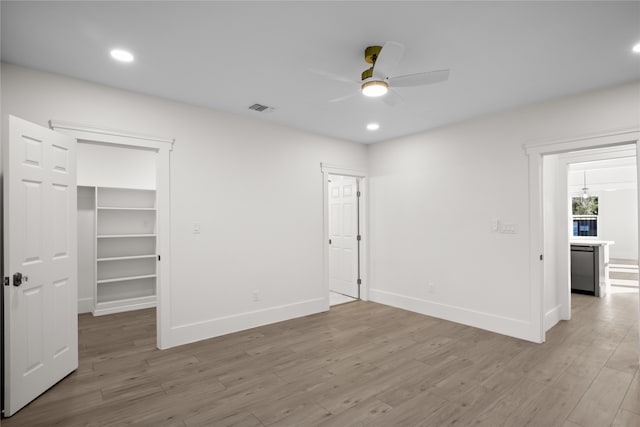 unfurnished bedroom with ceiling fan, light hardwood / wood-style floors, a walk in closet, and a closet