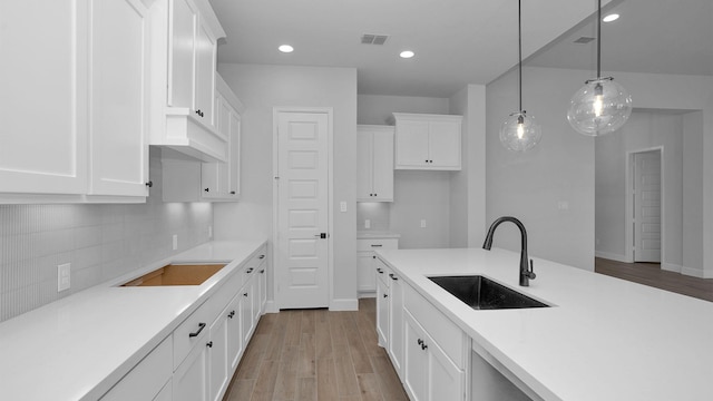 kitchen featuring sink, light wood-type flooring, pendant lighting, decorative backsplash, and white cabinets