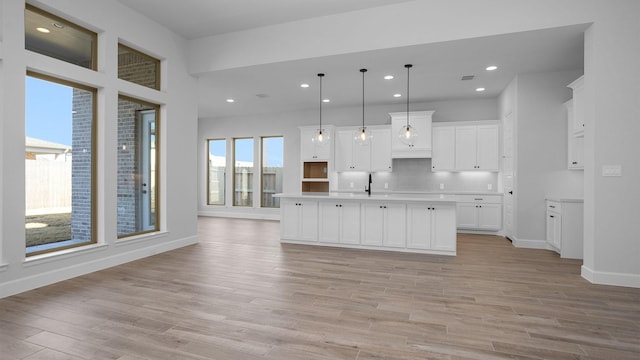 kitchen featuring sink, light hardwood / wood-style flooring, pendant lighting, a kitchen island with sink, and white cabinets