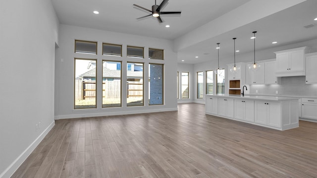 unfurnished living room with ceiling fan, sink, and light wood-type flooring