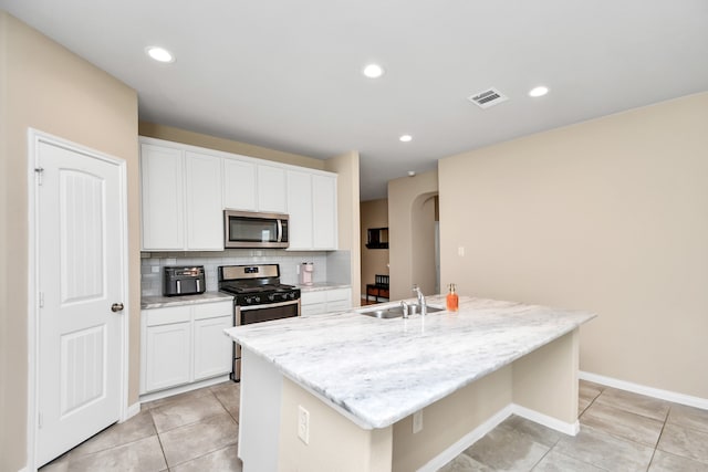 kitchen featuring appliances with stainless steel finishes, backsplash, a kitchen island with sink, sink, and white cabinets