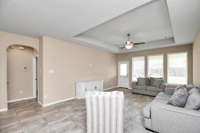 living room with a raised ceiling and ceiling fan