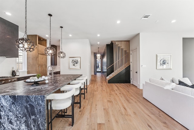 kitchen with a breakfast bar, hanging light fixtures, a kitchen island, and light hardwood / wood-style floors