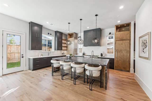 kitchen featuring a center island with sink, plenty of natural light, light wood-type flooring, and decorative light fixtures