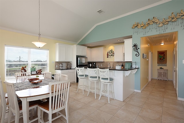 kitchen with a breakfast bar, backsplash, white cabinets, crown molding, and vaulted ceiling