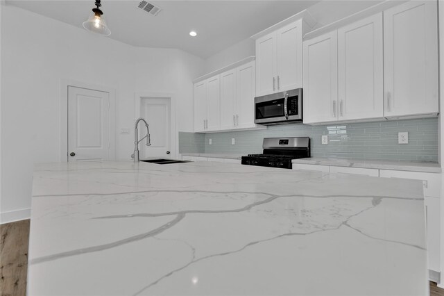 kitchen featuring light stone countertops, white cabinets, wood-type flooring, and appliances with stainless steel finishes