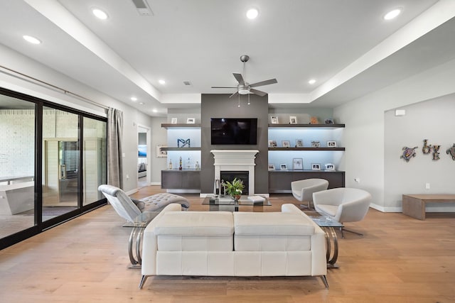 living room featuring a tray ceiling, ceiling fan, a fireplace, and light hardwood / wood-style floors