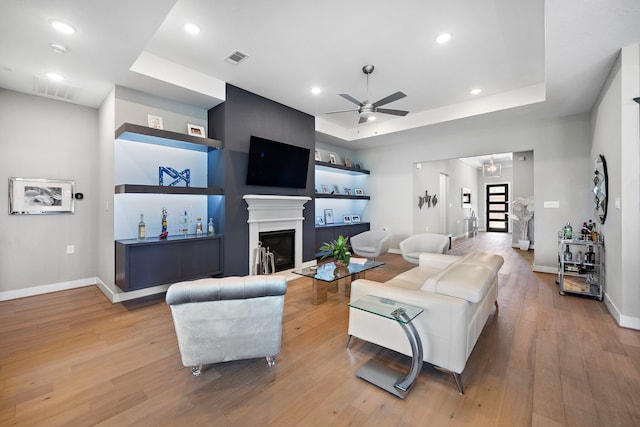 living room with a tray ceiling, light hardwood / wood-style flooring, and ceiling fan