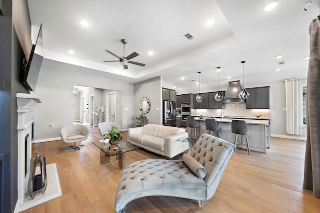 living room with light wood-type flooring, a tray ceiling, and ceiling fan