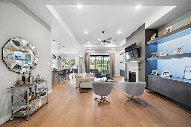 living room with ceiling fan, a raised ceiling, and light wood-type flooring