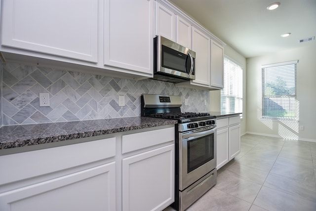 kitchen with white cabinets, appliances with stainless steel finishes, backsplash, and dark stone countertops