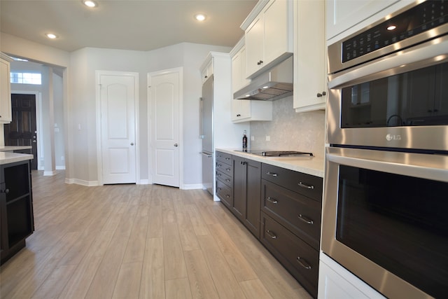 kitchen featuring white cabinetry, stainless steel appliances, tasteful backsplash, light stone counters, and light wood-type flooring