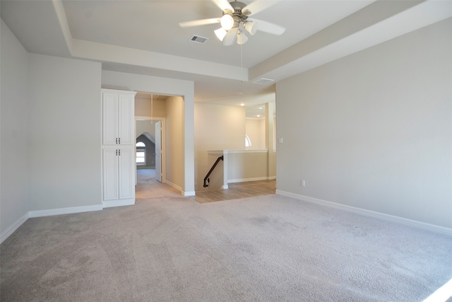 spare room with ceiling fan, light colored carpet, and a tray ceiling