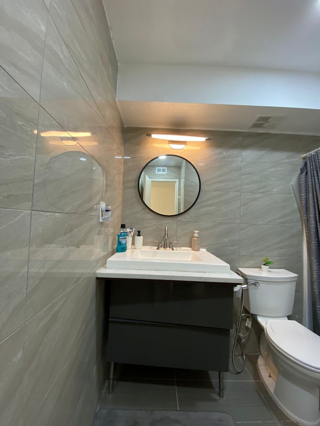 bathroom featuring toilet, vanity, tile patterned floors, and tile walls