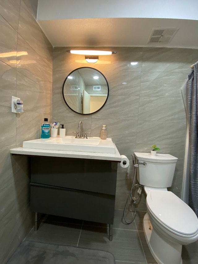 bathroom featuring tile patterned floors, vanity, toilet, and tile walls