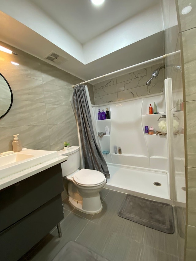 bathroom featuring walk in shower, vanity, tile walls, tile patterned flooring, and toilet