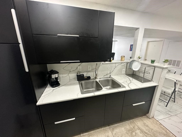 kitchen with decorative backsplash, light stone countertops, sink, and fridge