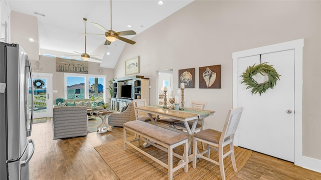 dining space with ceiling fan, light wood-type flooring, and high vaulted ceiling