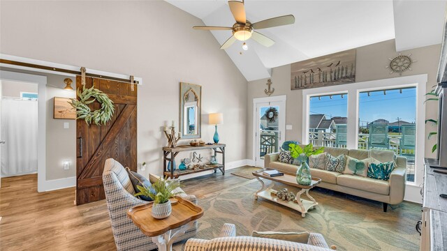 living room with hardwood / wood-style floors, ceiling fan, a barn door, and high vaulted ceiling