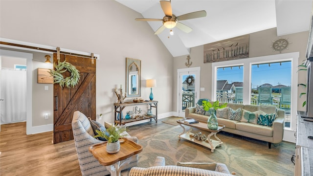 living room featuring hardwood / wood-style flooring, high vaulted ceiling, a barn door, and ceiling fan