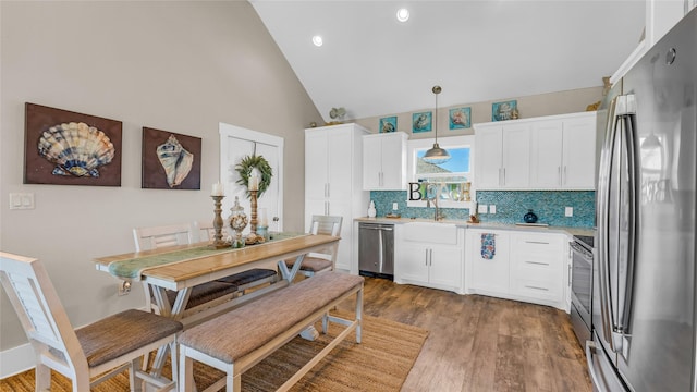 kitchen with stainless steel appliances, backsplash, hardwood / wood-style floors, pendant lighting, and white cabinets