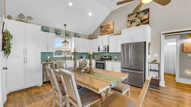 kitchen featuring appliances with stainless steel finishes, tasteful backsplash, decorative light fixtures, light hardwood / wood-style flooring, and white cabinetry